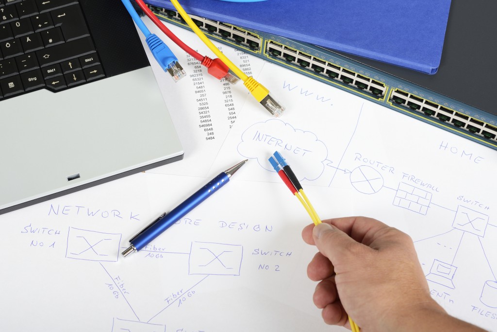 A hand holding a cable over a workspace of schematics of network cable drawings.